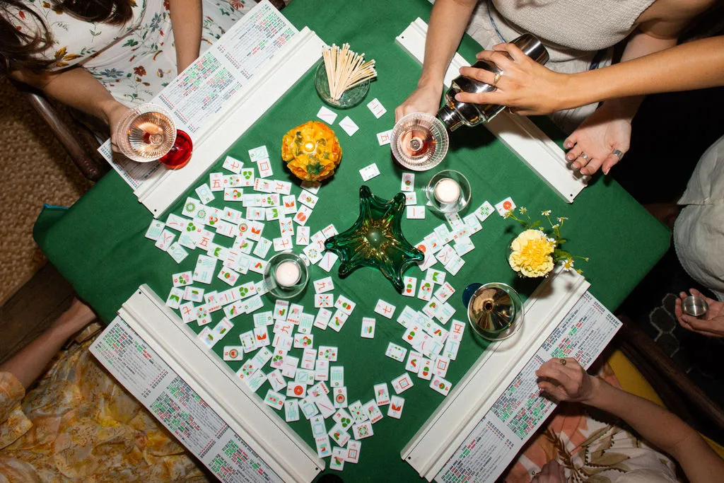 Friends enjoying mahjong and cocktails around a green table