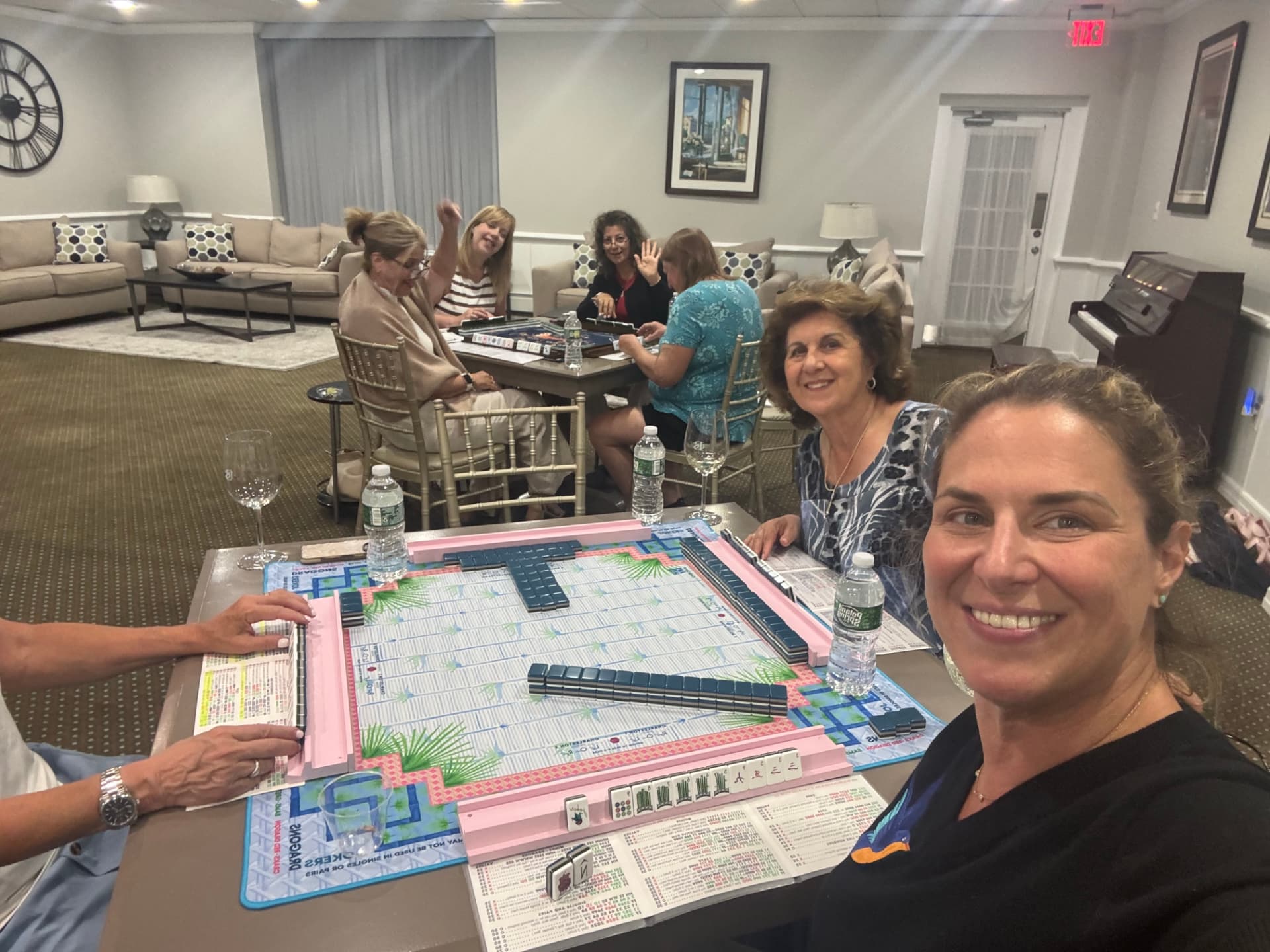 A full room of mahjong players waving happily from their tables as Sandra takes a selfie